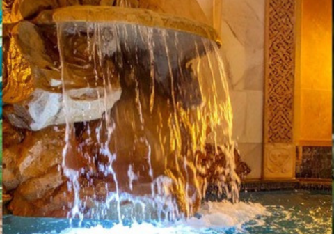 Close-up of a custom-built rock waterfall feature cascading over textured stone into a pool or basin, illuminated by warm underwater lighting, showcasing residential water features and pond design.
