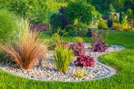 Professional landscape design featuring ornamental grasses, colorful Heuchera (coral bells), and a decorative gravel bed surrounded by lush green lawn.