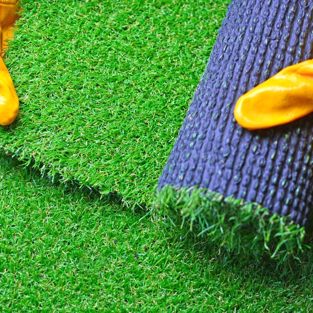 Close-up of an installer in yellow gloves unrolling a section of newly installed, vibrant green artificial grass (synthetic turf) with a dark backing, highlighting professional artificial grass installation services in Las Vegas.