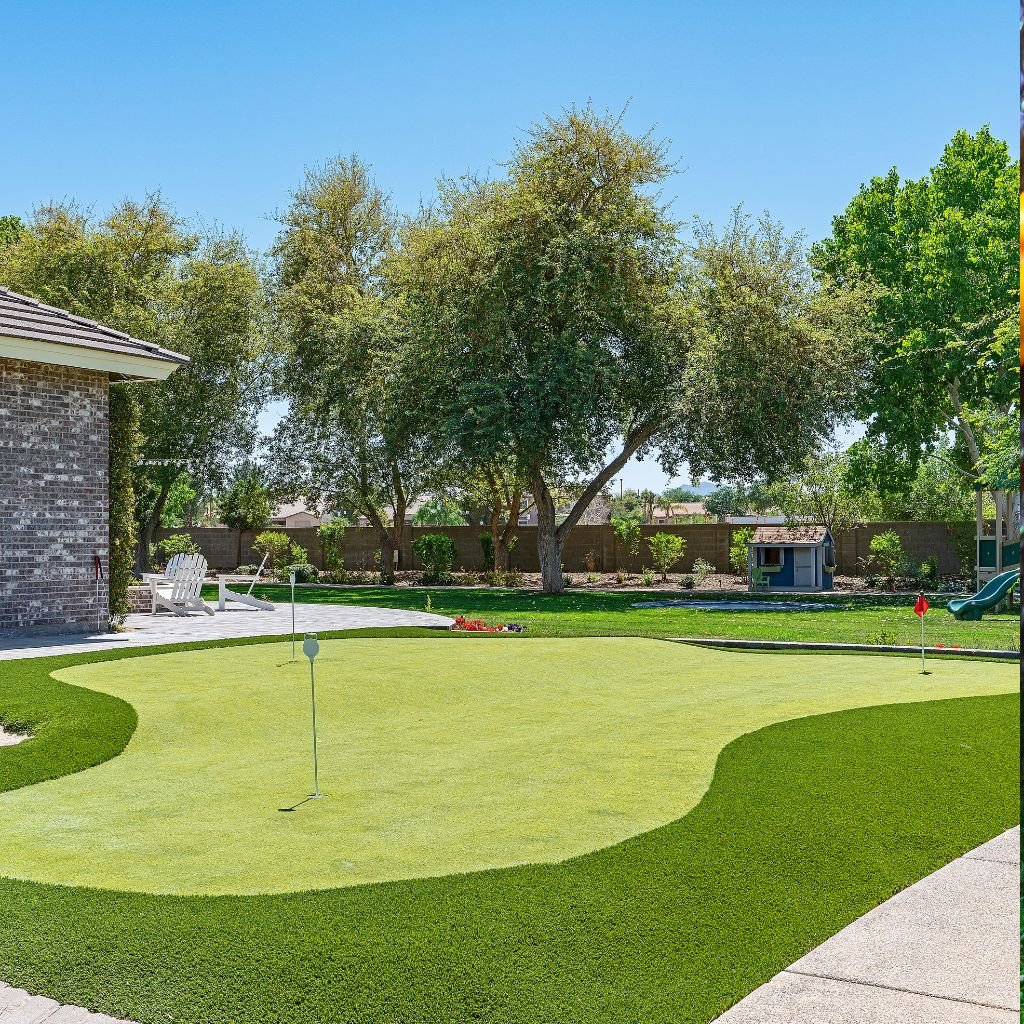 Residential backyard featuring a professionally installed artificial turf putting green with two cups and flags, surrounded by synthetic grass and mature trees, highlighting premium putting green installation services in Las Vegas.