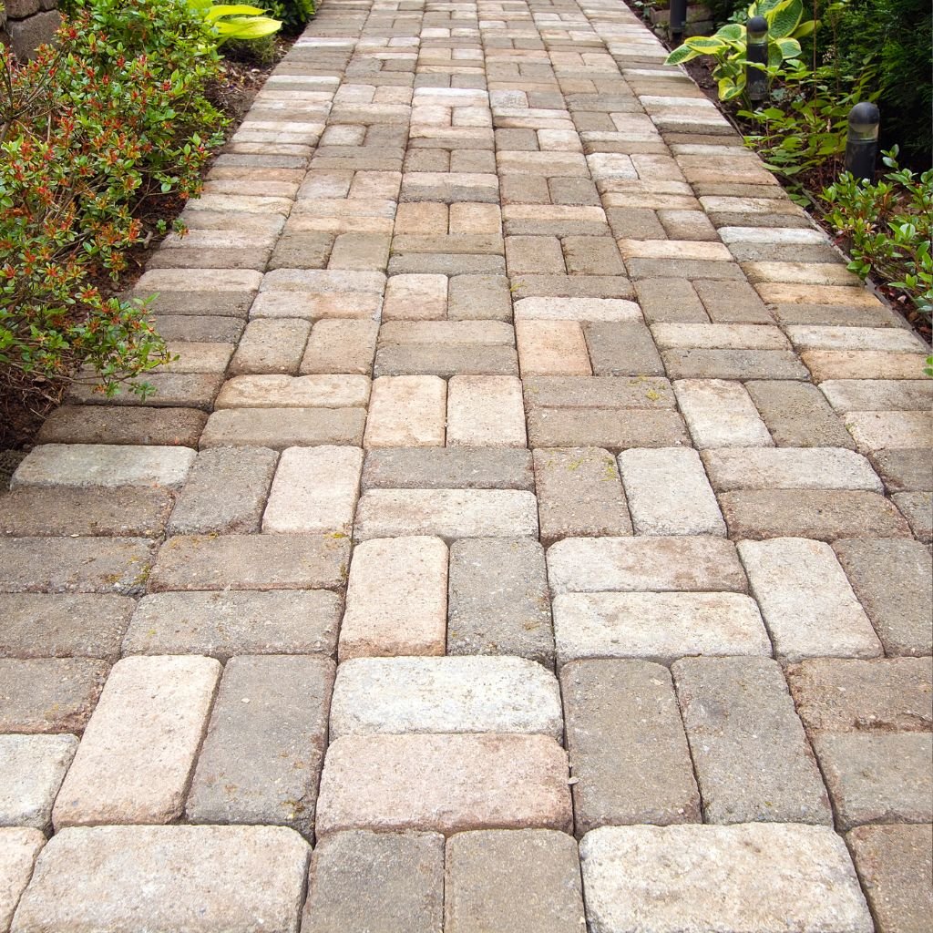 A well-maintained paver walkway installed in a 90-degree herringbone pattern, featuring rustic tan and grey rectangular paving stones bordered by landscaping, showcasing expert paver installation services in Las Vegas.
