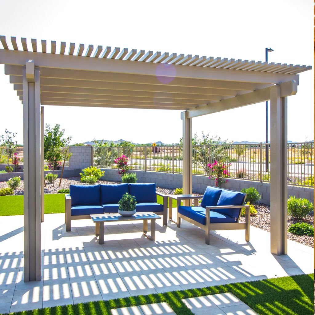 Modern, freestanding aluminum pergola with slatted roof providing shade over an outdoor lounge area, featuring blue cushion furniture on a white paver patio, showcasing professional pergola installation and design.